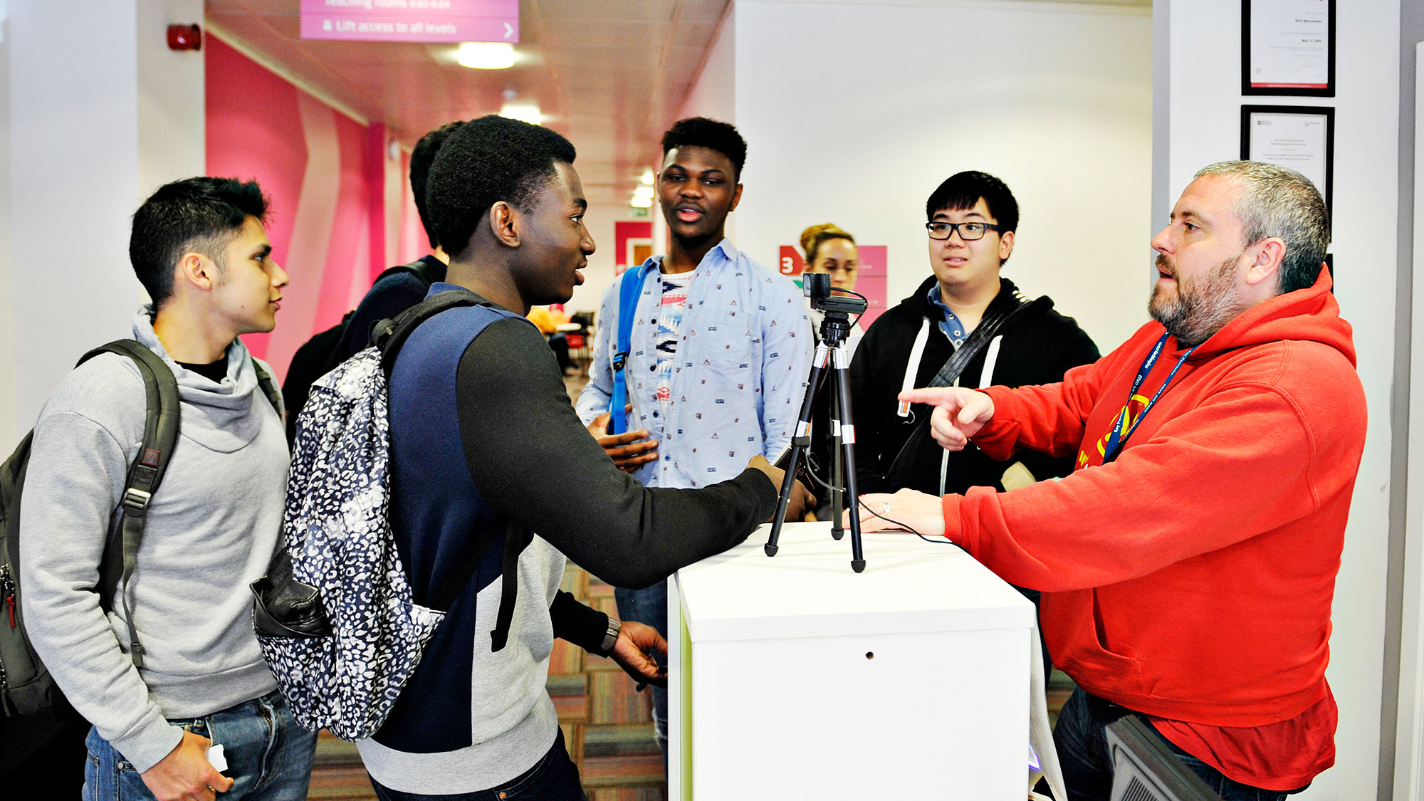 International students speak with instructor at desk with tripod in INTO Manchester Centre.